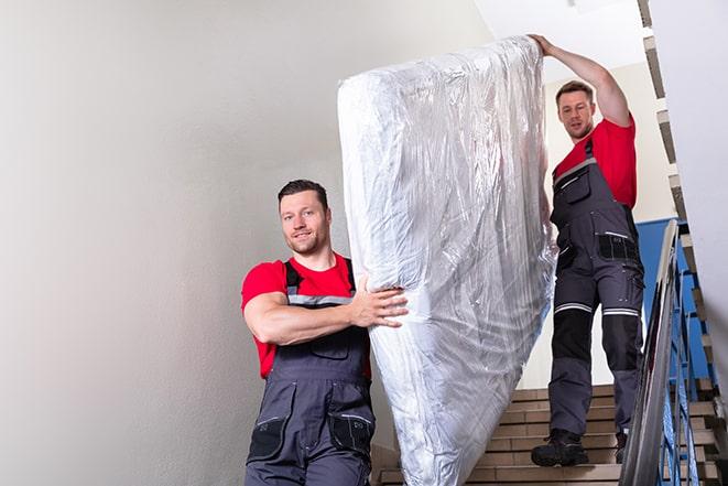 two people carrying a box spring out of a bedroom in Deer Park, TX